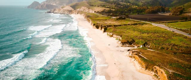 Aerial view of Half Moon Bay coastline with turquoise surf, wide sandy beach, and golden coastal cliffs, California