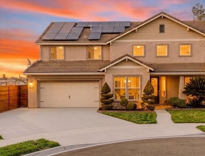 Two-story suburban home with solar panels, two-car garage, and illuminated windows at sunset